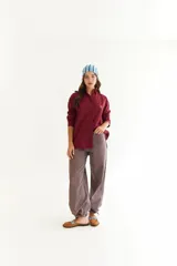 Camisa de corte oversize color bordó, con cuello camisero, mangas largas y bordado en hilo rojo en la espalda con la frase The Winter League. Presenta recortes con costuras a contratono y detalle de placa metálica pequeña en la parte superior trasera.