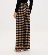 Pantalón de pijama de corte holgado confeccionado en franela con estampado de cuadros en tonos beige y negro. Presenta cintura elástica con botones decorativos en la parte frontal.