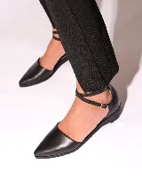 Zapato de cuero negro con punta fina y tira con hebilla alrededor del tobillo.