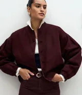 Campera estilo bomber de sarga color bordó, con cuello alto, cierre frontal con botones forrados, mangas largas con puños elásticos y bajo ajustado.