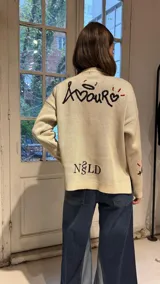 Campera tejida en hilo color crudo con diseño de corazón negro central, cierre frontal completo y detalles bordados en rojo y negro en mangas y cuerpo.