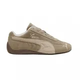 Zapatilla Puma de perfil bajo, estilo automovilismo, color beige/marrón claro con detalles en blanco. Presenta una capellada de gamuza, la icónica franja Puma en un tono más claro y suela de goma marrón oscuro.