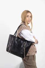 Cartera tipo tote bag de cuero vacuno marrón, con detalles de trenzado artesanal en los laterales y flecos colgantes decorativos. Cuenta con doble asa de hombro y cierre superior.