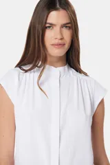Blusa blanca sin mangas, con cuello mao y cierre frontal oculto con botones.
