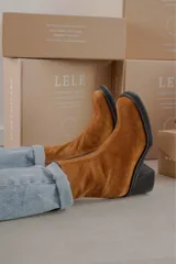 Bota de caña media con punta cuadrada, confeccionada en cuero gamuzado color marrón, con taco bloque y suela de goma negra.