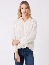 Camisa de algodón color gris con bordados florales en el frente y las mangas. Tiene cuello con solapa y cierre frontal con botones.