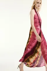 Vestido midi de cuello halter y escote en V, con diseño tie-dye en tonos fucsia, borgoña y verde. Presenta un nudo decorativo en el delantero, espalda descubierta y abertura frontal en el bajo.
