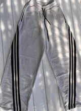 Pantalón deportivo color naranja con las icónicas tres rayas blancas laterales características de la marca Adidas.