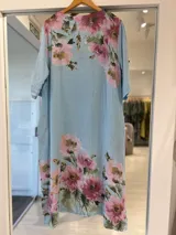 Vestido midi celeste de lino con estampado floral en tonos rosados y verdes, escote en V con cordones y apliques de argollas de madera, y mangas cortas con presilla.