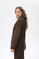 Blazer de ante color marrón con silueta oversize, cierre frontal con botones, bolsillos con solapa y tajo trasero. Presenta detalles de costuras con terminaciones pintadas a mano.