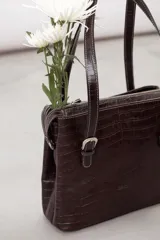 Cartera de hombro estructurada color negro, confeccionada en 100% cuero vacuno con textura en relieve tipo reptil. Cuenta con asas largas ajustables mediante hebillas metálicas plateadas, cierre superior y el logo de la marca grabado en la parte frontal.