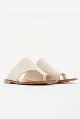 Sandalias chatas de cuero color off-white, con diseño minimalista de tira ancha asimétrica y presilla para el dedo.