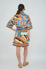 Vestido corto de algodón con estampado geométrico a rayas en tonos marrón, celeste, azul y negro, con cuello camisero, mangas tres cuartos y cinturón ajustable del mismo género.