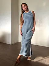 Vestido largo de punto sin mangas, color gris con rayas verticales blancas y destellos de lurex dorado. Presenta cuello redondo y abertura lateral en el dobladillo.