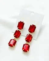 Aros colgantes con tres gemas rectangulares de color rojo rubí engarzadas en metal dorado.