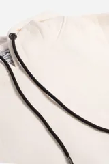 Canguro de felpa color crudo con capucha y bolsillo tipo canguro. Presenta un estampado pequeño en el pecho y un parche con logo en la manga izquierda.