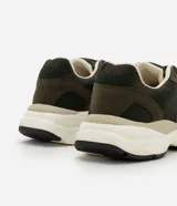 Championes deportivos de diseño urbano, confeccionados en una combinación de poliuretano y poliéster con acabado tipo gamuza. Presentan una silueta con recortes superpuestos, cierre de cordones, entresuela volumosa en tono crema y suela de goma.