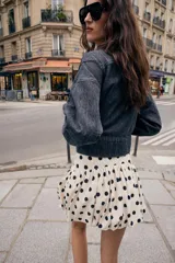 Falda pantalón de estilo globo con diseño abullonado y estampado de lunares negros sobre fondo crudo. Presenta cintura alta y cierre lateral con cremallera oculta.