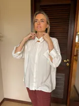 Camisa de corte clásico y calce holgado, color blanco, con cuello camisero, cierre frontal de botones ocultos y mangas largas con puños abotonados.