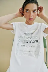 Camiseta de algodón con cuello redondo y manga corta. Presenta un diseño estampado frontal con efecto metalizado plateado sobre fondo rectangular.