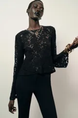 Top de encaje negro con cuello redondo, manga larga y hombreras incorporadas. Presenta un diseño de corte recto y cierre posterior.