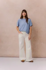 Pantalón jean de tiro alto y corte wide leg, color off white. Presenta un diseño minimalista con bolsillos funcionales, cierre frontal con botón y detalles metálicos plateados.