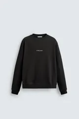 Sudadera de cuello redondo y manga larga, confeccionada en algodón con interior afelpado. Presenta un diseño de corte regular con estampado de texto en contraste en la parte frontal y acabados en rib en puños y ruedo.