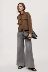 Campera negra de efecto gamuzado con cuello camisero, cierre frontal de botones, bolsillos plaqué en el pecho y detalles de costuras decorativas y calados.