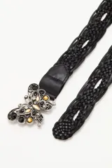 Cinturón de cuero trenzado color negro con hebilla metálica decorativa en forma de mariposa, adornada con piedras negras, doradas y cristales.