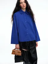 Camisa oversize de lyocell color tostado, con cuello clásico, cierre frontal de botones y mangas largas con puños anchos. Presenta un diseño de corte relajado con caída fluida.