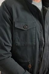 Campera verde militar de algodón y elastano, con cierre frontal de botones y cremallera, cuatro bolsillos delanteros con solapa y cordón ajustable en la cintura. Forro interior de viyela de algodón a cuadros.