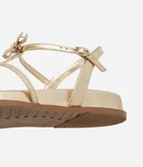 Sandalia plana dorada con tiras finas y detalle de lazos.