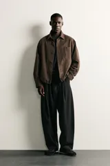 Pantalón de corte balloon fit en color gris oscuro, confeccionado en tejido con viscosa. Presenta pliegues frontales, cintura ajustable con cinturón integrado, bolsillos laterales y bolsillos traseros de doble vivo. Cierre frontal con cremallera y botón.