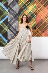 Vestido amplio de lino y algodón, con escote recto y tiras finas. Su corte evasé y los recortes de tela generan una silueta con mucho volumen y movimiento. Estampado de líneas a cuadros en tonos grises y blancos.