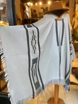 Poncho gris claro de hilo de algodón con diseño geométrico en negro y detalles de flecos en los bordes.
