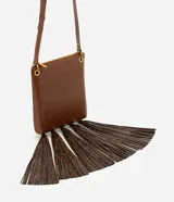 Bolso tipo postman de tamaño mediano en color marrón, con cierre superior y correa ajustable. Presenta un diseño rectangular con múltiples borlas largas en la parte inferior con estampado animal print.