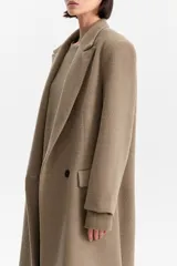 Tapado largo de silueta recta en color tostado, con hombros estructurados y solapas clásicas. Presenta bolsillos laterales con solapa y cierre frontal de dos botones.