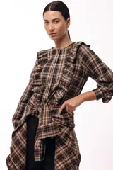 Camisa de manga larga con estampado de cuadros en tonos tierra, cuello redondo y cierre frontal con botones. Presenta volados verticales en el frente y un detalle de lazada en la cintura que permite entallar la prenda.