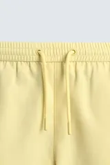 Bañador corto de hombre color amarillo pálido, confeccionado en tejido técnico con acabado aterciopelado. Presenta cintura elástica ajustable con cordón, bolsillos laterales y un bolsillo trasero de plastrón con solapa. Incluye forro interior.