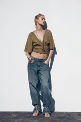 Sandalia plana color beige con tira para el dedo y tira delantera con detalle de abalorios metálicos. Cierre mediante tira con hebilla en el tobillo y acabado en punta redonda.