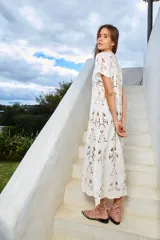 Vestido largo color crudo, con cuello redondo y manga corta. Confeccionado en tela de encaje de algodón con diseño floral y tajo lateral.