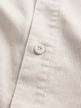 Camisa de pana color beige, de corte recto, con cuello clásico, cierre frontal de botones y un bolsillo en el pecho.