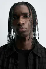 Camisa negra de corte relajado con tejido semitransparente de estructura abierta y patrón a cuadros. Presenta cuello solapa, manga corta, bolsillo plastrón en el pecho y cierre frontal de botones.