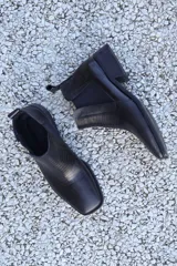 Bota corta de cuero negro con elástico lateral, punta fina y taco bajo.