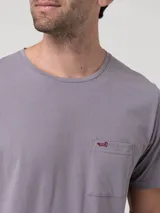 Remera de cuello redondo y manga corta en color gris, con un bolsillo aplicado en el pecho que presenta un pequeño bordado de un pato en color contrastante.