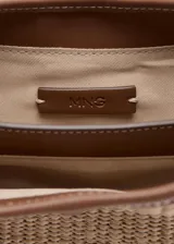 Bolso tipo bucket de canvas y efecto piel, con base, asas y detalles en marrón. Cuenta con una trabilla frontal con candado metálico dorado y cierre magnético.