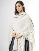 Ruana de punto color beige con sutiles motas multicolores, con bordes terminados en flecos largos.
