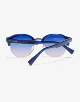Gafas de sol Hawkers unisex, con montura azul y lentes degradadas de azul a rosa.