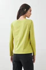 Remera de manga larga color verde lima, con escote redondo y detalle de bordados calados en forma de pico en la zona del pecho.
