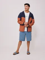 Campera rompevientos con cierre frontal, confeccionada en nylon con diseño de bloques de color en tonos verde azulado y gris claro. Cuenta con capucha, puños elásticos y cordón de ajuste en el ruedo.